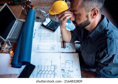 Overworked stressed Man engineer having headache while working on his project blueprint at work. Frustrated male with tension sitting at desk full of drawings - Powered by Shutterstock
