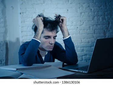 Overworked and Stressed young student preparing exams late at night on laptop feeling distressed fatigued tired worried and sad. Moody dark light. Online learning, University education and stress.