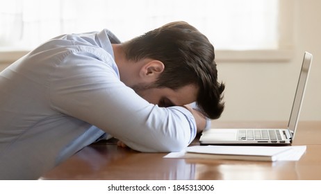 Overworked. Too tired exhausted young man freelancer businessman student working studying from home lying on desk sleeping at workplace before pc screen being overloaded by hard work difficult task