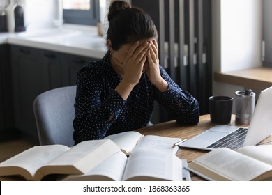 Overworked. Tired young indian lady sit at home desk crowded with books hide face in palms feeling headache migraine. Exhausted female student feeling bad losing concentration unable to learn study - Shutterstock ID 1868363365