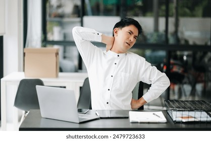 Overworked young Asian businessman office worker suffering from neck pain after had a long day at her office desk. office syndrome concept - Powered by Shutterstock