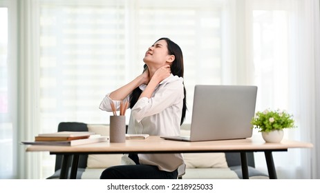 Overworked young Asian businesswoman or female office worker suffering from neck pain after had a long day at work, massaging her neck. office syndrome concept