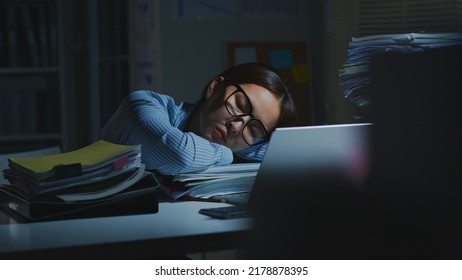Overworked young Asian office employee sleeping while working on laptop computer overtime in office at night - Shutterstock ID 2178878395
