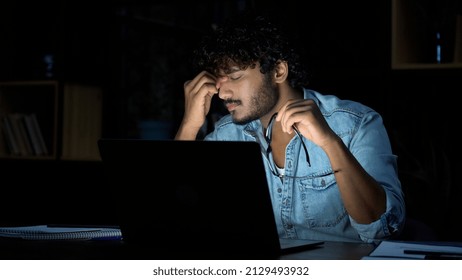 Overworked young indian businessman taking off glasses working late at night. Tired sleepy stressed student holding eyeglasses feeling lack of sleep, having eyestrain problem, using laptop computer. - Shutterstock ID 2129493932