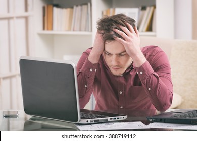 Overworked young man sitting at the desk and holding his head