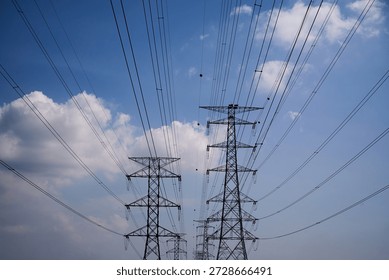 ow angle view of high voltage electricity transmission towers (pylons) with multiple power lines stretching across the sky. Energy infrastructure and utility grid concept with dramatic perspective.