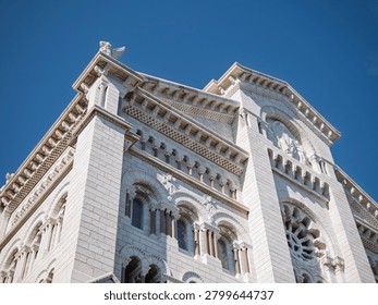 ow angle view of the Saint Nicholas Cathedral facade in Monaco, framed by green trees, a classic street lamp, and people in the foreground under a clear blue sky.