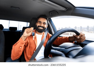 Own Automobile. Proud Car Owner Indian Man Showing His New Auto Key Driving Vehicle, Sitting In Driver Seat With Hands On Steering Wheel, Smiling To Camera. Dreams Come True
