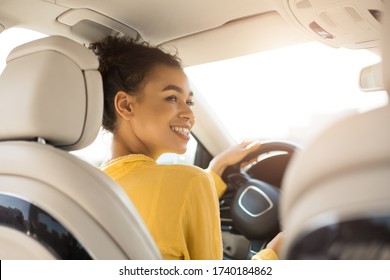Own Car. Cheerful Black Woman Driving Auto Sitting In Driver's Seat In Automobile. Back View, Selective Focus