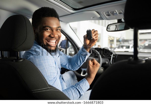 Own Car. Joyful\
African American Guy Holding Auto Key Shaking Fists Sitting In\
Automobile In Dealership\
Shop