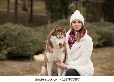 The owner is a beautiful girl in an artificial fur coat with her red husky dog. Beautiful portrait. Concept: love between dog and owner. Protection of animals.