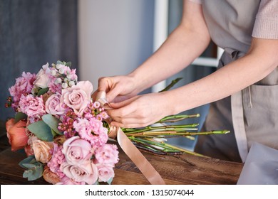 Owner of florist shop or studio tying beige silk ribbon around bunch of fresh pastel roses on table