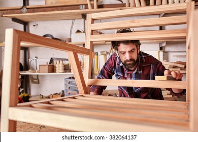 Owner Of An Independent Furniture Design And Manufacturing Business, Working On A Wooden Chair Frame That He Has Made In His Woodwork Studio, Carefully Sanding It Smooth