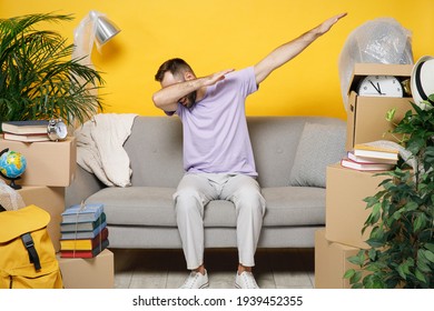 Owner Man Doing Dab Hip Hop Dance Gesture Sits In Living Room On Sofa At Home Household Unpacking Stuff In Polythene Indoor Rents Flat Isolated On Yellow Wall. Relocation Moving In Apartment Concept