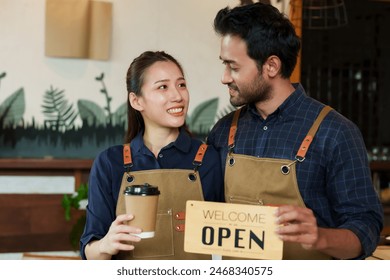 Owner small cafe, business couple Beautiful Asian woman holding coffee mug standing smiling men different nationalities. man embracing woman holding sign saying welcome open. Insidestore front counter - Powered by Shutterstock