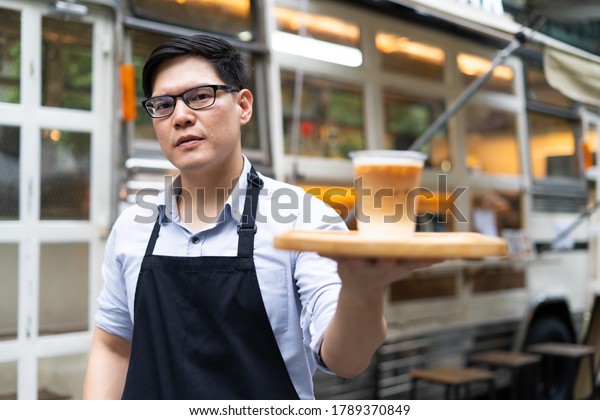 The owner of a small coffee shop welcomes\
customers in front of the coffee shop with a smile and a cup of\
coffee in hand. SME Business owner\
concept.
