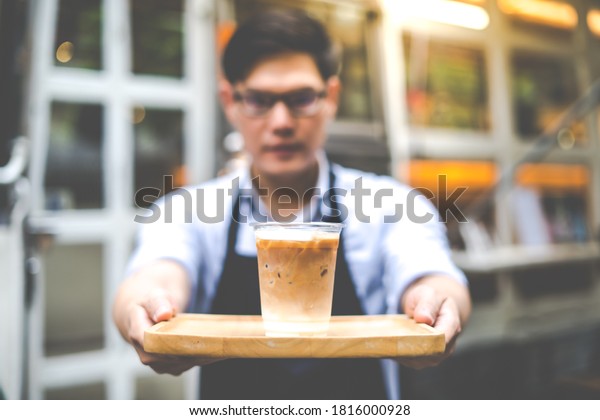 The owner of a\
small coffee shop welcomes customers in front of the coffee shop\
with a smile and a cup of coffee in hand. SME Business owner\
concept. Focus on the coffee\
cup