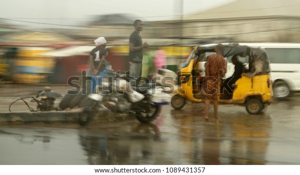 Oworonshoki,Lagos/Nigeria - 12th May,2018:\
Three people, a motorcycle and a scooter by the road in Nigeria\
after the rain. Taken from inside a car with blurry\
background.
