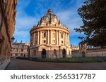 Oxford, UK - Radcliffe Camera bathed in golden sunlight, showcasing historic neoclassical architecture and surrounding academic charm on a clear day