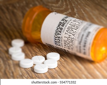 Oxycodone is the generic name for a range of opoid pain killing tablets. Prescription bottle for Oxycodone tablets and pills on wooden table for opioid epidemic illustration