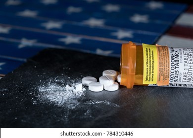 Oxycodone is the generic name for a range of opoid pain killing tablets. Prescription bottle for Oxycodone tablets and pills on slate table with USA flag in background
