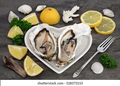 Oysters on a heart shaped plate with lemon fruit, parsley, an antique silver fork, shells and driftwood on marble.