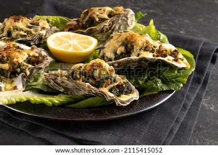 Oysters Rockefeller baked with spinach and cheese, served on a dark plate with lemon and lettuce, selected focus, narrow depth of field