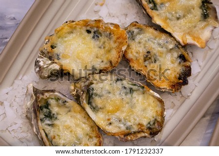 Oysters Rockefeller baked in spinach cream and parmesan sauce served on white plate. (Top View)