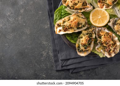 Oysters Rockefeller style baked with spinach and cheese on a plate with lemon and lettuce, dark slate background with copy space, view from above