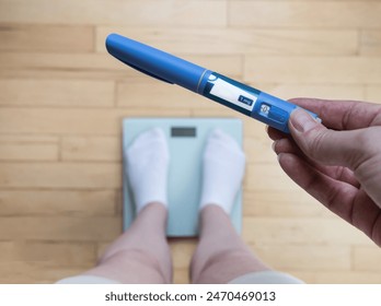  Ozempic Insulin injection pen for diabetics and weight loss. Woman weighs herself and holds Ozempic in her hand. Weight loss concept. - Powered by Shutterstock