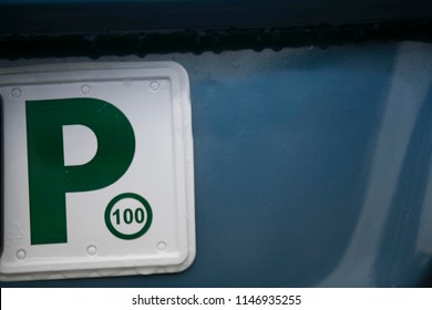 P Plate Sign Written With Blue With White Background Attached On The Back Of Green Car 