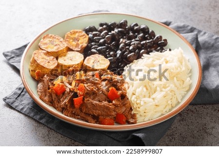 Pabellon criollo is a traditional dish of Venezuela with black beans, rice, plantains and shredded steak that have been cooked with tomatoes closeup on the plate on the table. Horizontal
