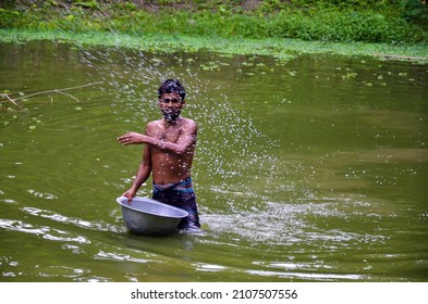 Pabna, Bangladesh - July 24, 2012: Man Throwing Fertilizer In The Pond For The Fish. An Adult Man With A Big Bowl Floating On The Water With Full Fertilizer Giving For The Fish To Feed. 