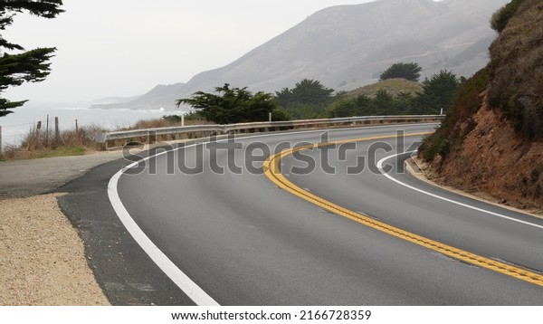 Pacific coast highway 1, Cabrillo road along\
ocean, foggy California, Big Sur, USA. Coastal road trip, traveling\
on car by sea. Cloudy misty weather. Yellow dividing line, asphalt.\
Turn of serpentine.
