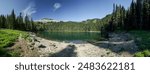 Pacific Crest Trail. A beautiful lake surrounded by trees and rocks. The sky is clear and blue; and the sun is shining brightly. The scene is peaceful and serene; with the water reflecting the sky