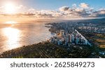 The Pacific Ocean waves roll to the sandy beach of Waikiki, Honolulu, Hawaii, USA. Aerial view on the city at sunset. Cloudy sky at backdrop.