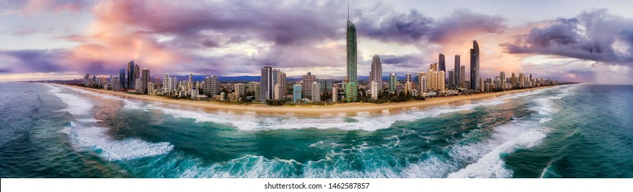 Pacific ocean waves rolling ashore of Surfers paradise suburb on Australian Gold Coast at sunrise with active board surfers riding the waves in front of high-rise towers.