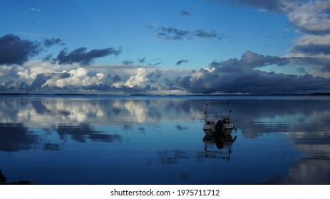 Pacification of nature. The sky and clouds are reflected in the smooth surface of the water. The boat is afloat.