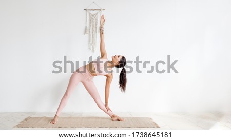 Pacified young well-groomed brunette asian woman doing stretching while standing Extended Triangle pose, Utthita Trikonasana. in a pink gymnastic suit on a white background. Place for advertising