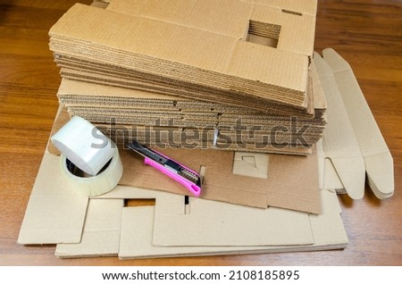a pack of disassembled boxes for packaging, adhesive tape and a clerical knife on the table. Tools for product packaging. Packing for the delivery of goods. collection of online orders.