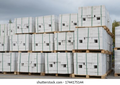 Pack of white silicate bricks on wooden pallets against the blue cloudy sky. Closeup stack in 3 rows.