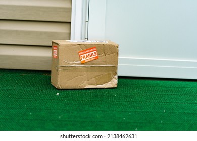 A Package Outside A Residential Door With A Fragile, Handle With Care Sticker On The Cardboard Carton.