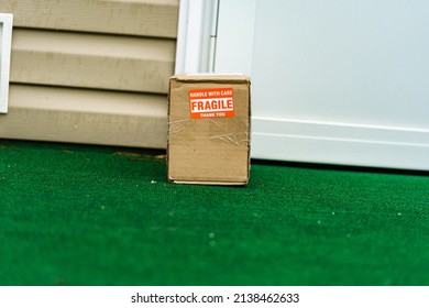 A Package Outside A Residential Door With A Fragile, Handle With Care Sticker On The Cardboard Carton.