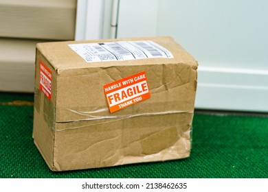 A Package Outside A Residential Door With A Fragile, Handle With Care Sticker On The Cardboard Carton.