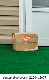 A Package Outside A Residential Door With A Fragile, Handle With Care Sticker On The Cardboard Carton.