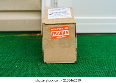 A Package Outside A Residential Door With A Fragile, Handle With Care Sticker On The Cardboard Carton.