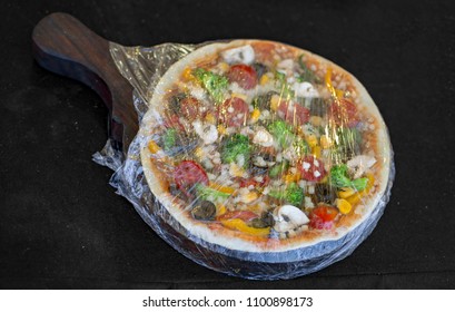 Packaged And Wrapped Homemade Pizza In Plastic Wrap With Wooden Base