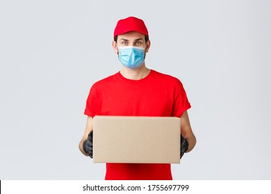 Packages and parcels delivery, covid-19 self-quarantine delivery, transfer orders. Young courier in red uniform, gloves and face mask, holding box, give-out order to client, contactless service - Shutterstock ID 1755697799