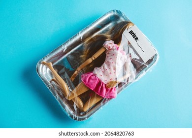 Packaging covered with food wrap with female doll inside. Inscription price. Concept of human trafficking. Conceptual stock photo. Top view on  blue background.
