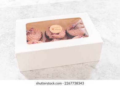 Packaging freshly baked chocolate strawberry cupcakes garnished with gourmet mini pink chocolates into a white paper cupcake box. - Powered by Shutterstock